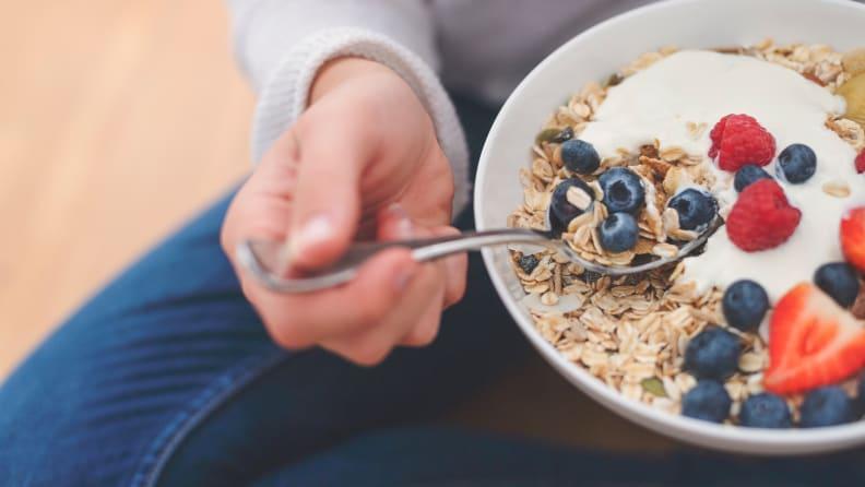 A bowl of yogurt, fruit, and granola being held by someone.