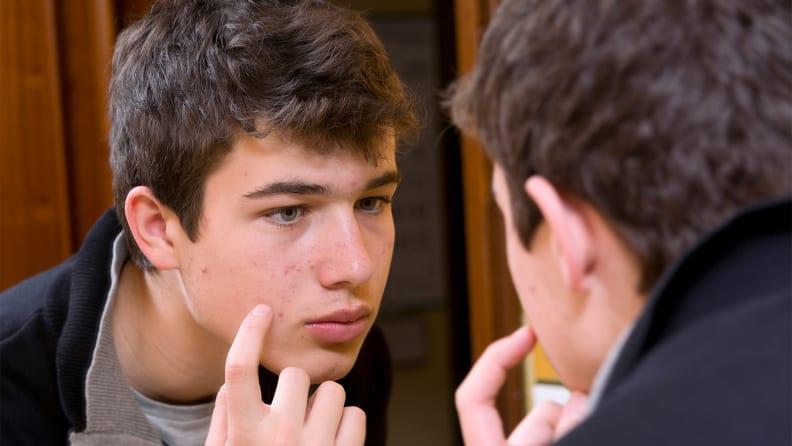 A young man looking into a mirror and touching his face.